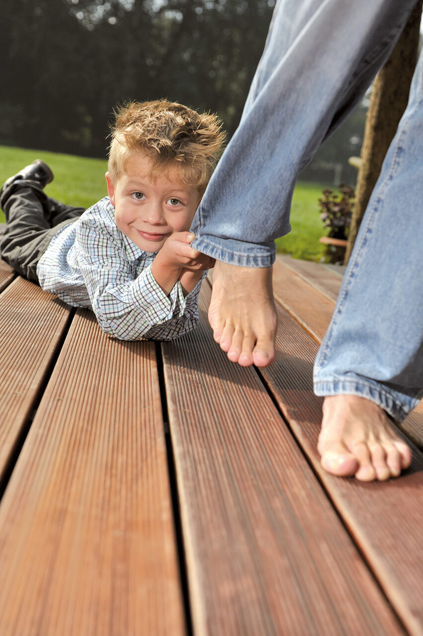 Kind spielt mit Mutter auf dunklen Terrassendielen aus Holz
