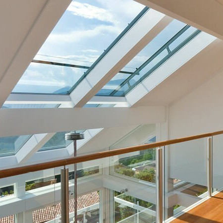 Modernes Dachgeschoss mit großen Glasdachfenstern, Holzfußboden und Glasgeländer, lichtdurchflutet mit Panoramablick.